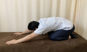 正座して手を前に伸ばして腰のストレッチしている上山和俊の写真