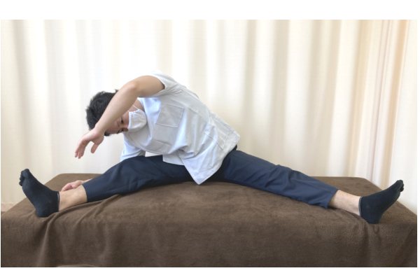 上山和俊が左腰の後ろのズキズキする痛みを改善するために、開脚して側屈のストレッチをしている写真